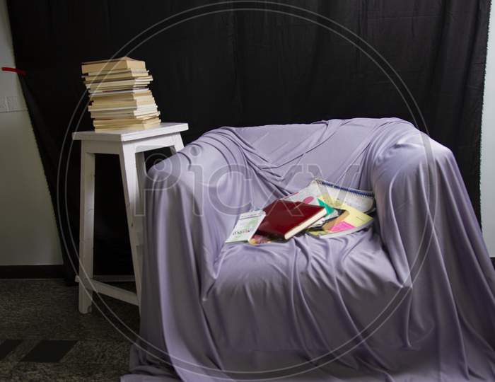 There Are Some Books On The Sofa Chair. And Books Are Placed On The Side Table.