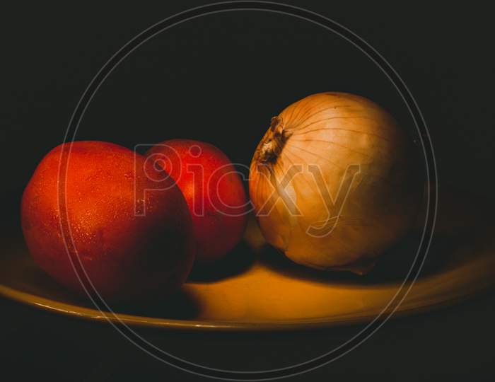 Tomatoes And Onion On A Yellow Plate With Dark Background. Light Painting Photography And Long Exposure.