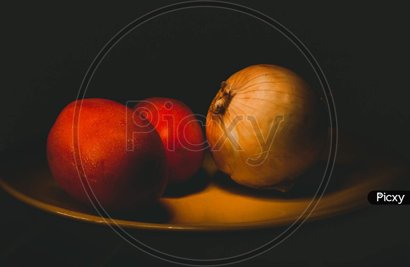 Tomatoes And Onion On A Yellow Plate With Dark Background. Light Painting Photography And Long Exposure.