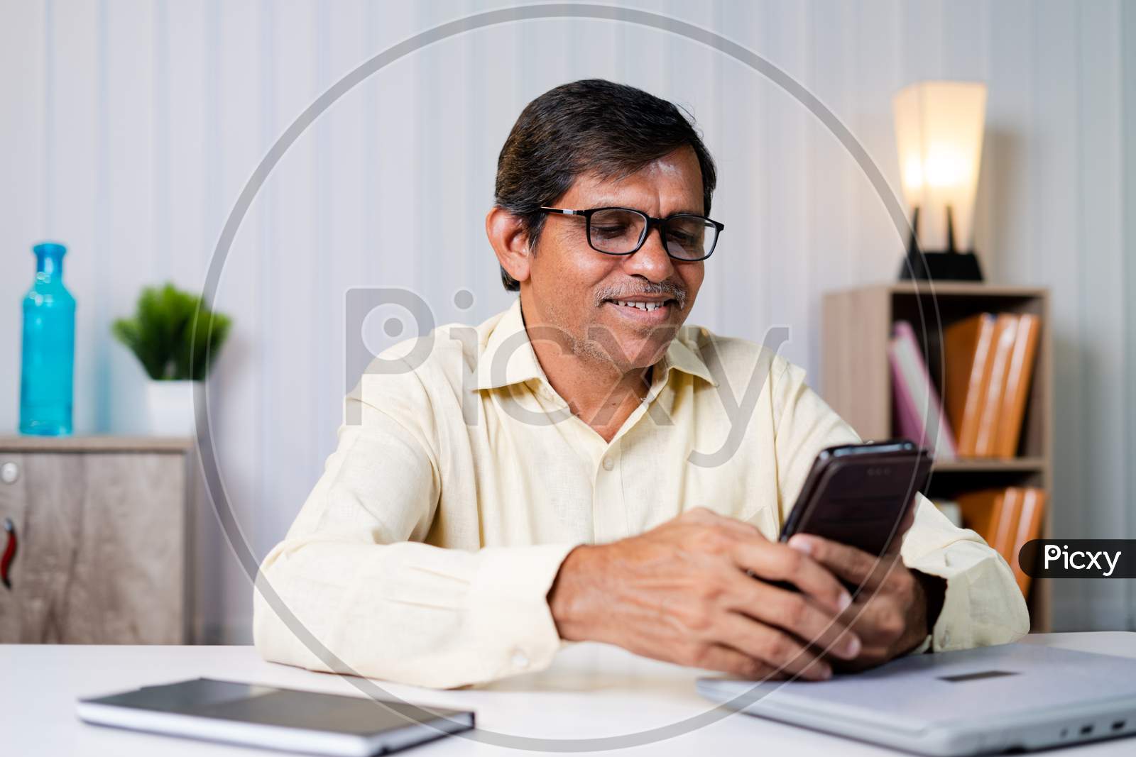 Middle Aged Businessman Smiling While Using Mobile Phone At Office - Concept Of Using Social Media, Internet, Checking Mails And Communication At Workplace