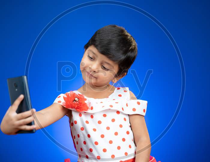 Little Girl Kid Or Toddler Taking Selfie And Checking Photos From Mobile Phone On Blue Background - Concept Of Technology, Internet And Modern Lifestyle