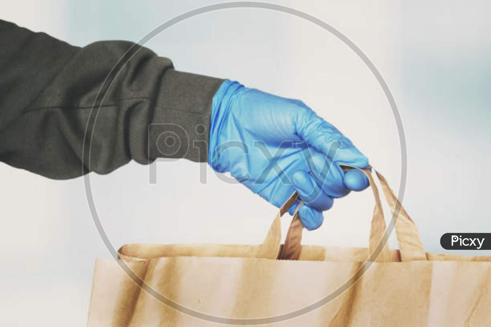 Delivery Person Hand Wearing Blue Protective Glove Giving Paper Bag. Online Shopping During Coronavirus Pandemic, Courier Grocery Delivery