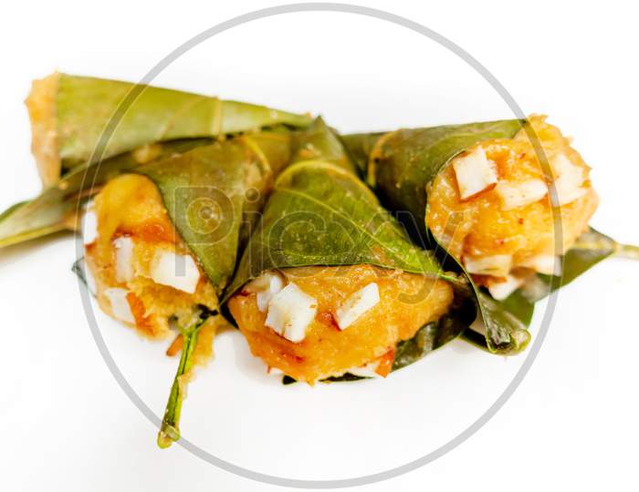 Traditional steamed ripe palmyra palm fruit cake wrapped with jackfruit leaves and sprinkled with coconut pieces. Steamed palmyra palm cake in isolated white background.