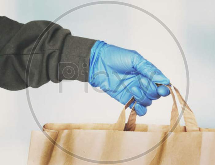 Delivery Person Hand Wearing Blue Protective Glove Giving Paper Bag. Online Shopping During Coronavirus Pandemic, Courier Grocery Delivery