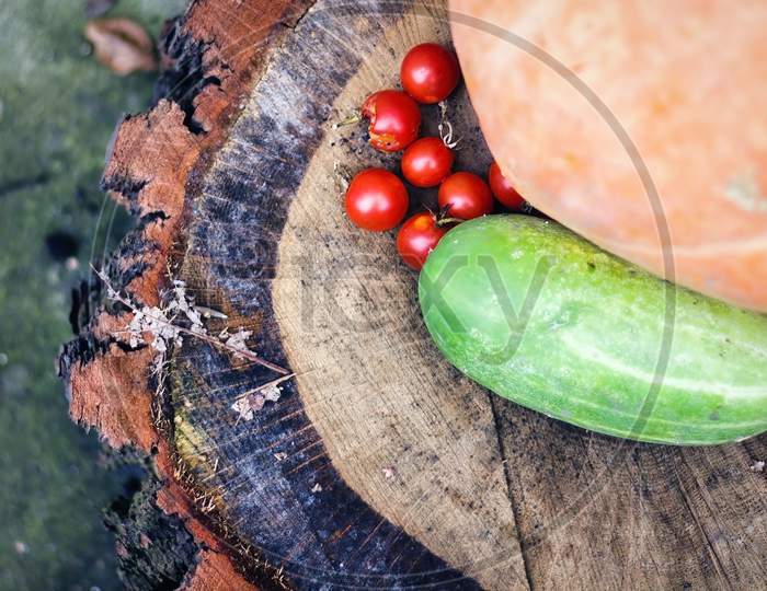 Mix Of Different Vegetable On A Wooden Log Such As, Cucumber, Pumpkin And Tomato On Wooden Chopped Table. Vegetables Harvest Gardening Concept