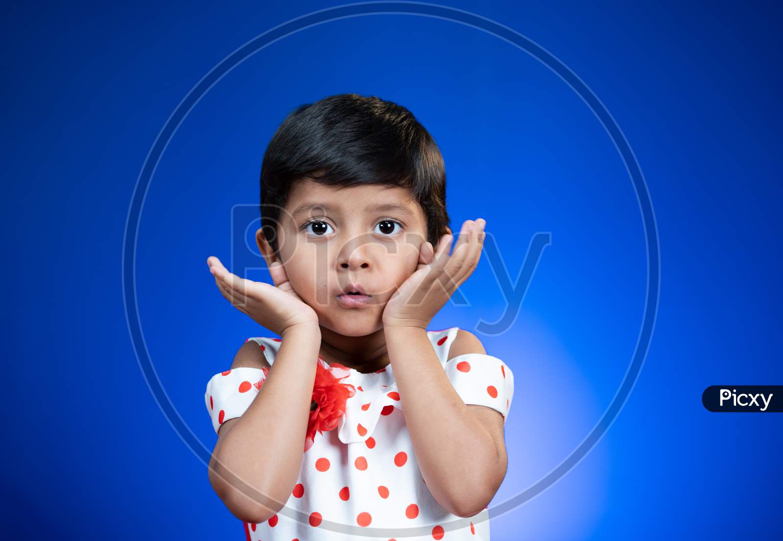 Cute Surprised Girl Kid Saying Wow By Closing Mouth With Hands And Looking At Camera On Blue Background - Concept Of Crazy Deal Or Offers.