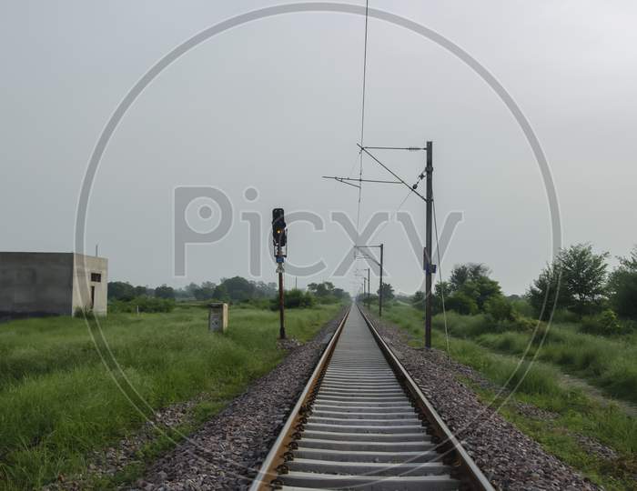 RAILWAY TRACK WITH LIGHT AND ELECTRIC POLE IN LANDSCAPE.