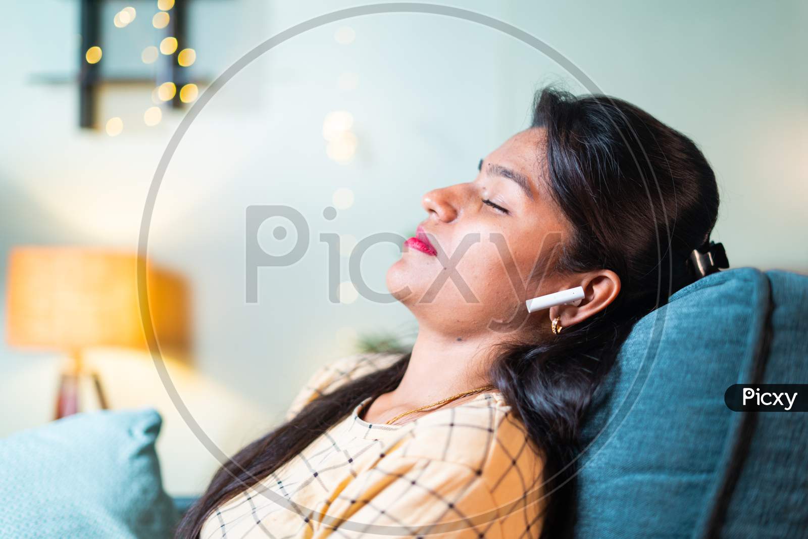 Young Girl With Closed Eyes Resting By Leaning On Sofa By Listening Favourite Song On Wireless Headphone In Living Room - Concept Of Taking Break,Relaxaing Or Spending Free Time By Enjoying Music