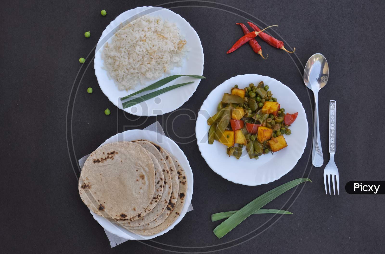 Top view of matar paneer mix veg, rice and chapati (Indian bread) on white plate over black background with copy space