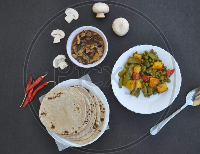 High angle view of matar paneer mix veg, mushroom soup and roti (Indian bread) over black background with copy space with copy space