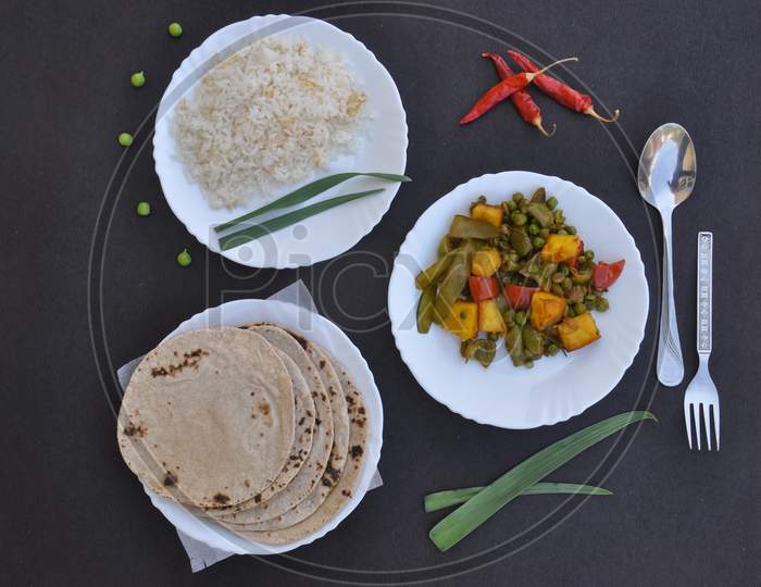 Top view of matar paneer mix veg, rice and chapati (Indian bread) on white plate over black background with copy space