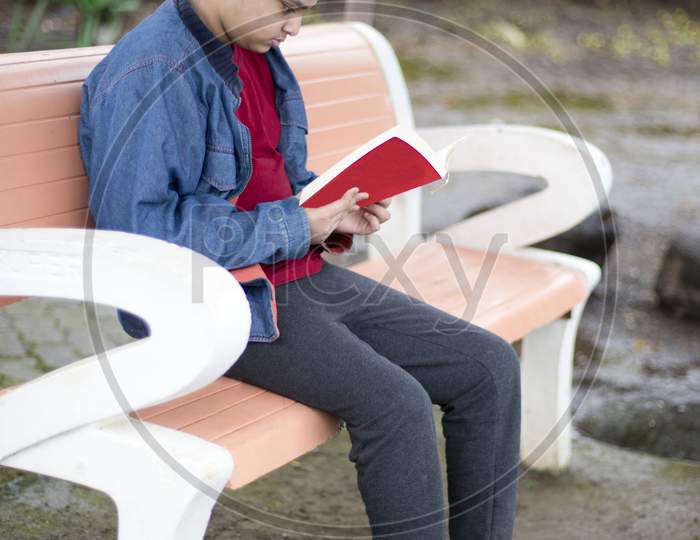 Young Boy Sitting On A Bench And Reading A Book