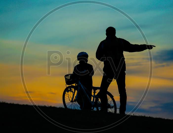 Silhouette Of Parent And Child Standing On Sunset Hill