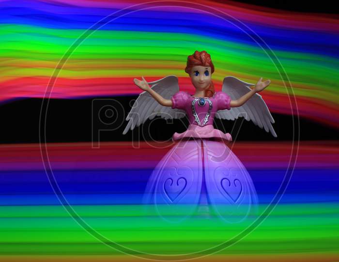 Colorful Light Painting Infront And Behind The Beautiful Angel Doll On The Black Background