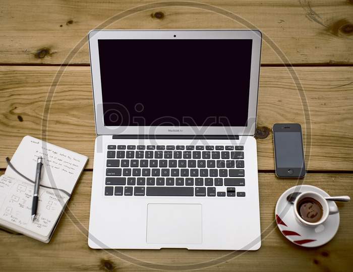 White laptop, back mobile, black tea and notebook with pen.