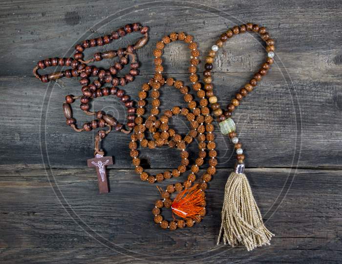 Set Of Rosaries Of Various Religions On Rustic Wood