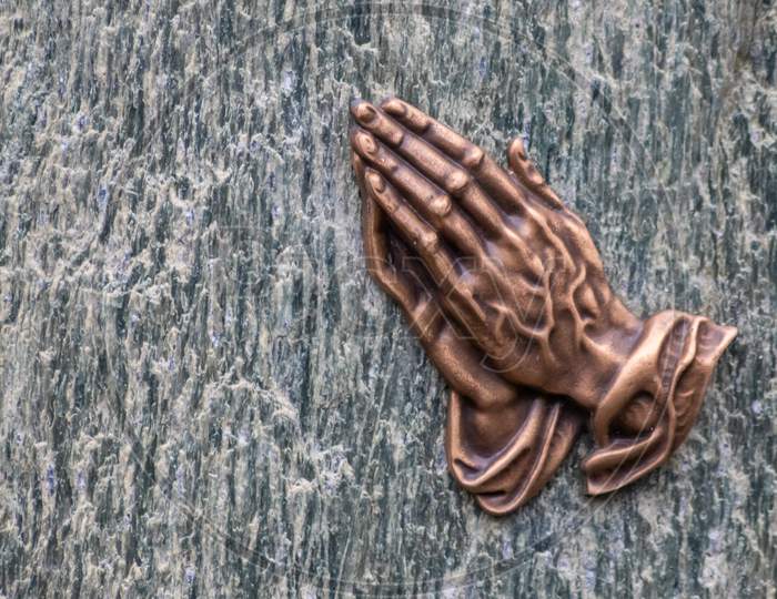 Praying hands as bronze figure on a graveyard grave as religious symbol for faith christianity blessing catholic priest and belief or confession with forgiveness for sinners or hope for saints believe