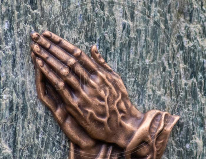 Praying hands as bronze figure on a graveyard grave as religious symbol for faith christianity blessing catholic priest and belief or confession with forgiveness for sinners or hope for saints believe