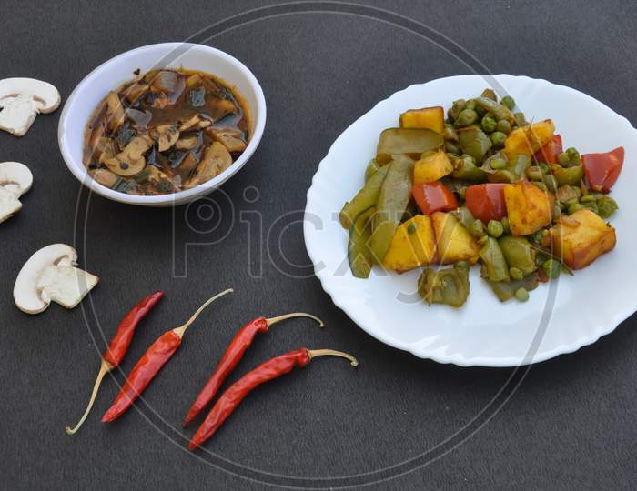 Flat lay of matar paneer veg and mushroom soup with red chillies over black background.