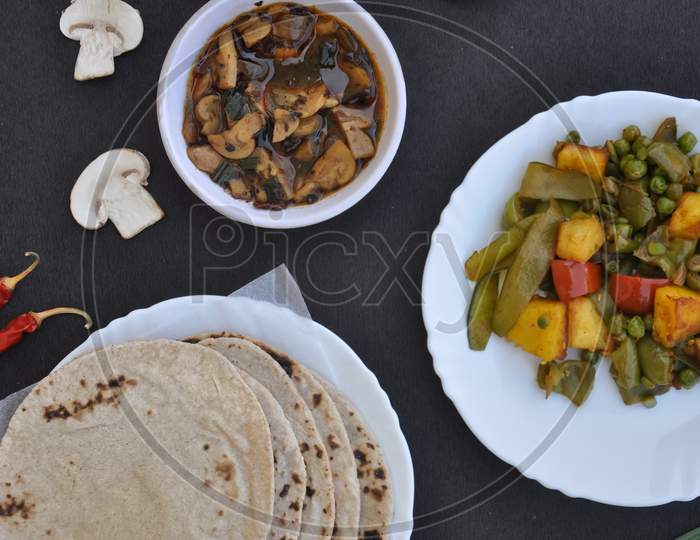 Top view of matar paneer mix veg, mushroom soup and roti (Indian bread) over black background.