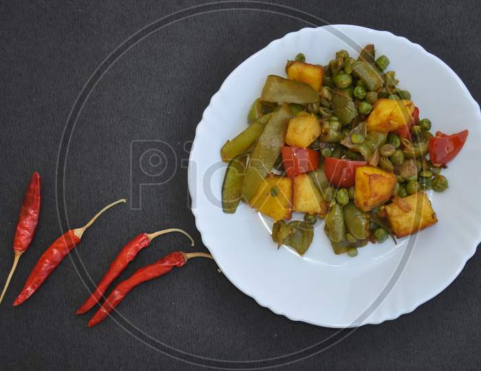Indian food - Flat lay of matar paneer mix veg recipe and red chillies over black background with negative space