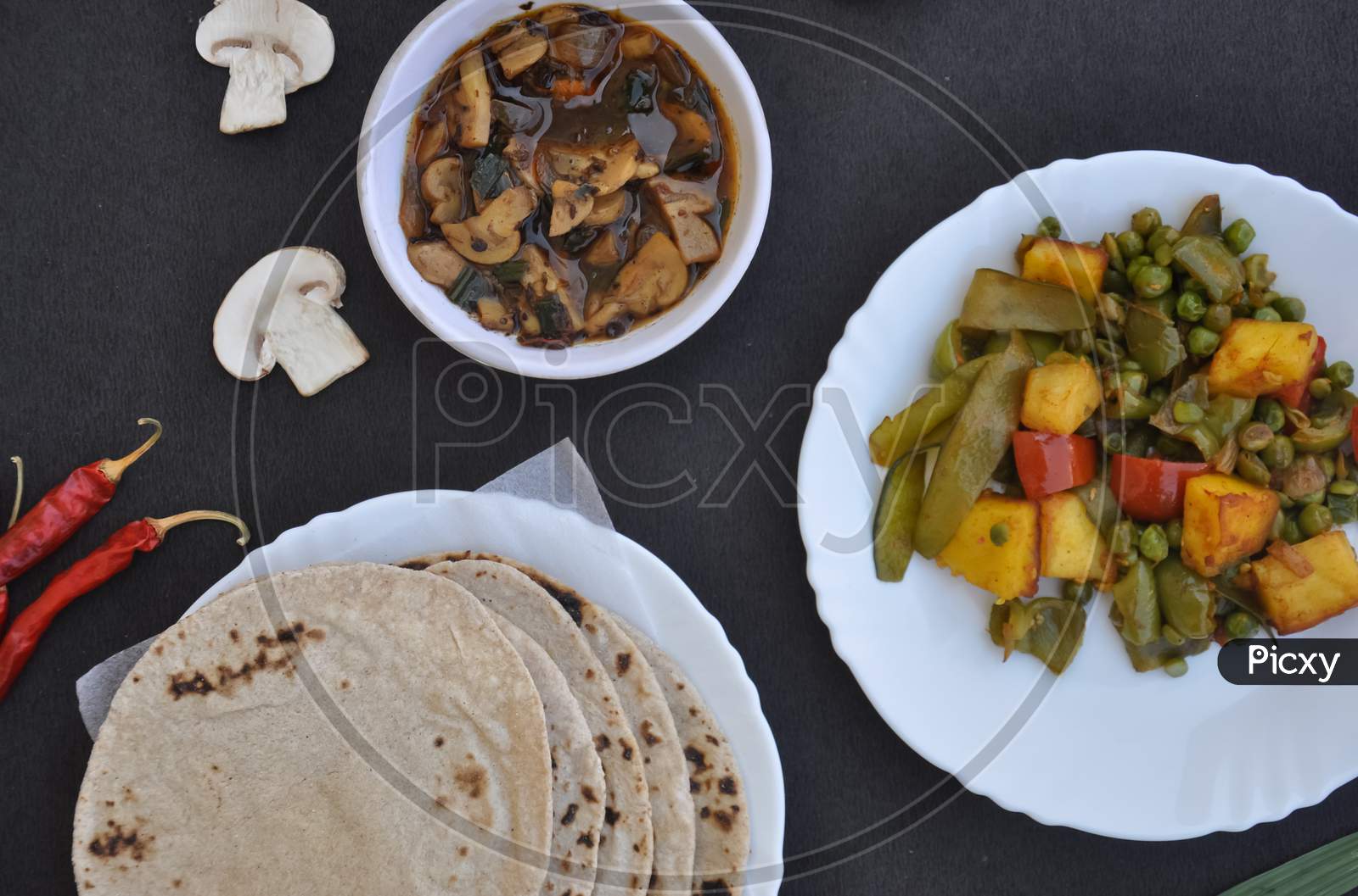 Top view of matar paneer mix veg, mushroom soup and roti (Indian bread) over black background.