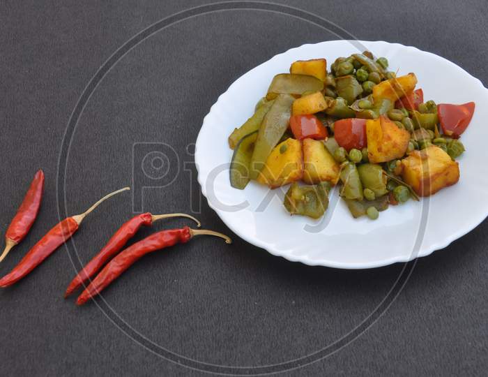 Indian food - Flat lay of matar paneer mix veg recipe and red chillies over black background with negative space