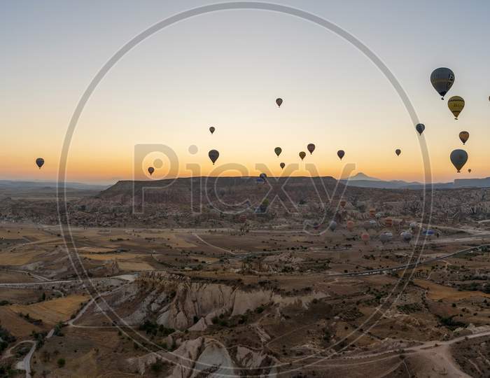 Cappadocia, Turkey - September 14, 2021: Wide Angle Panorama Aerial Shot Of Colorful Hot Air Balloons Together Floating In The Sky At Early Morning In Goreme Against Volcanic Hills