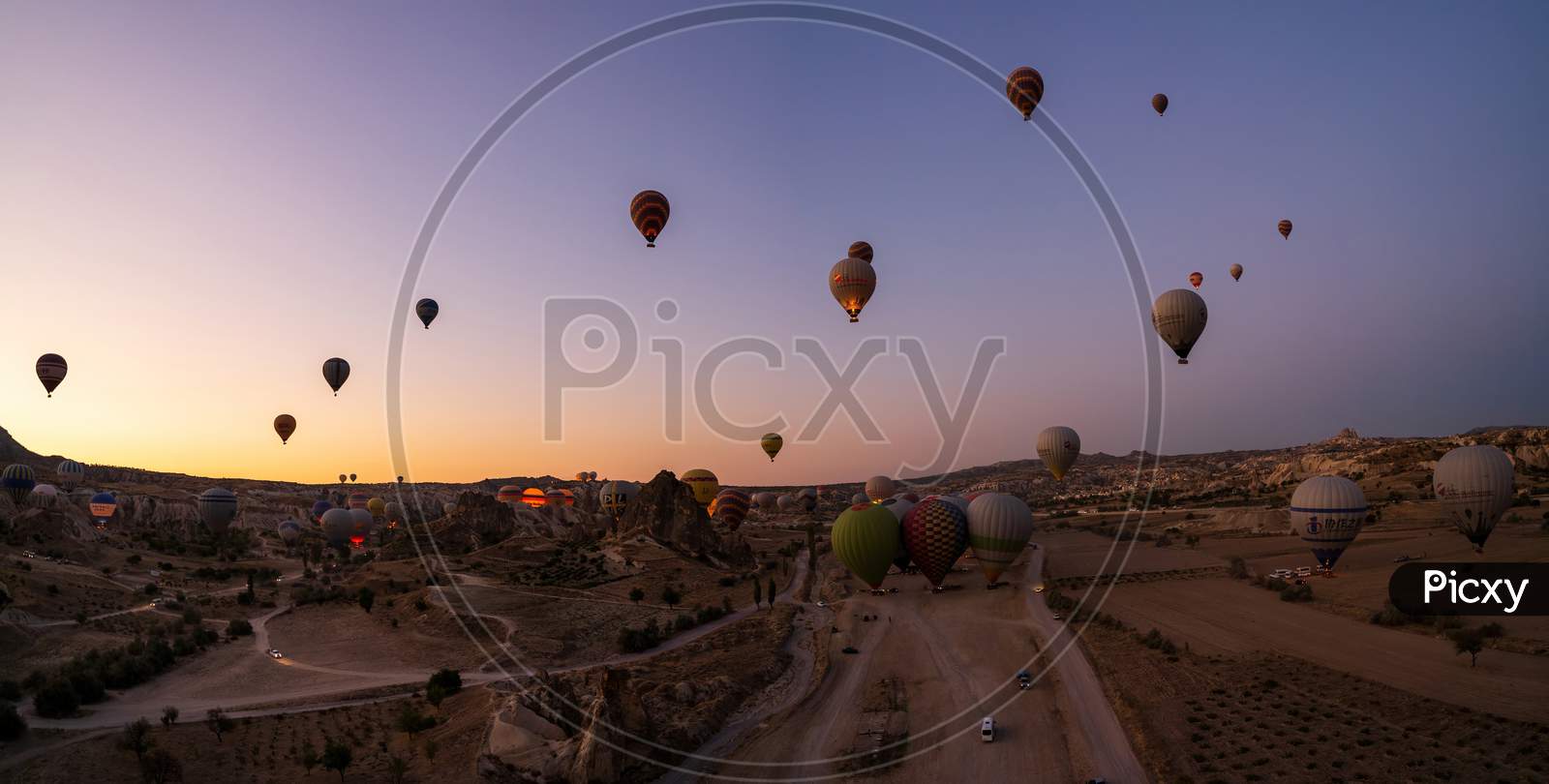 Cappadocia, Turkey - September 14, 2021: Wide Angle Panorama Aerial Shot Of Colorful Hot Air Balloons Together Floating In The Sky At Early Morning In Goreme