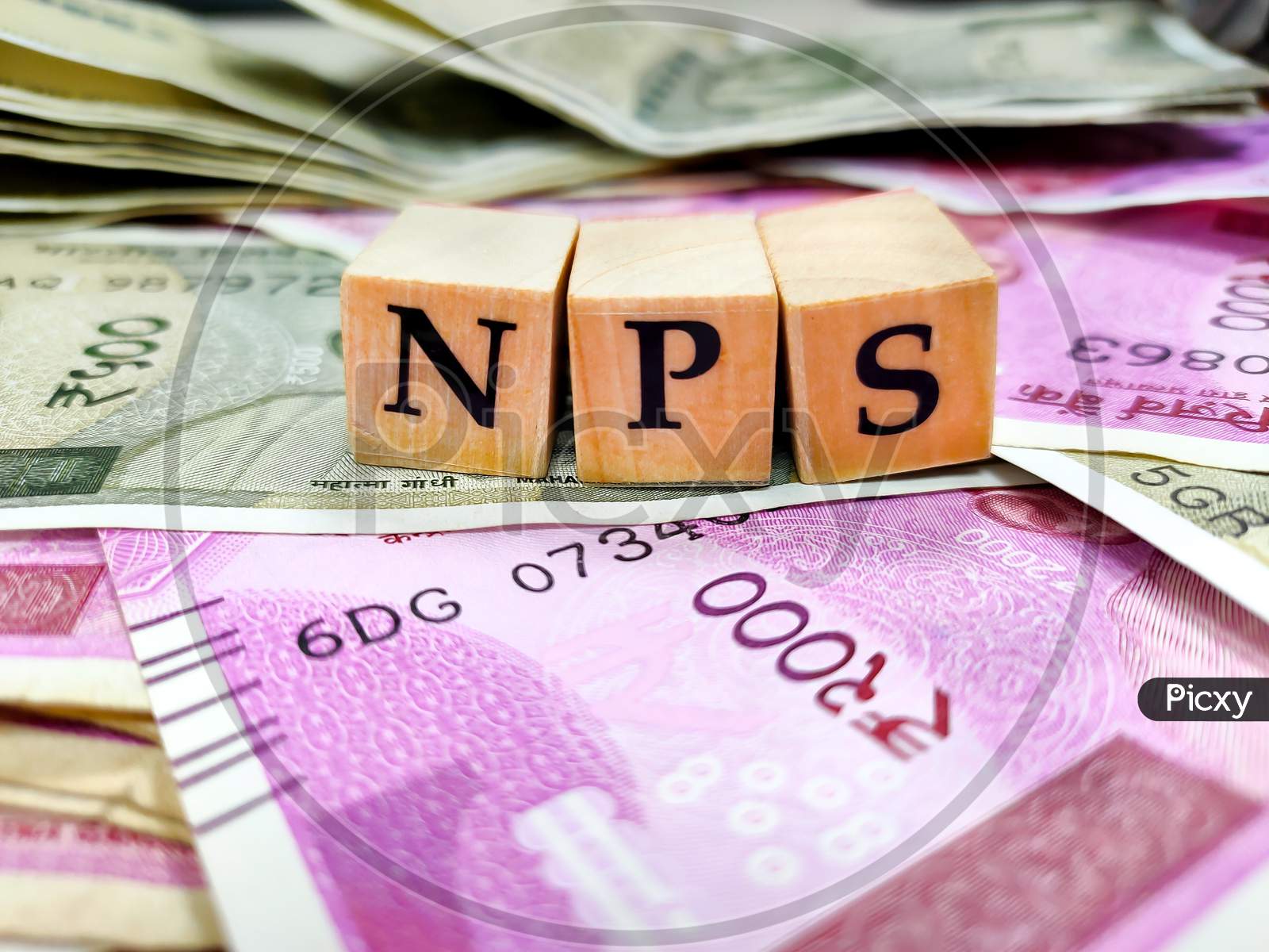 Nps Or National Pension Scheme With Wooden Bids Or Blocks On Indian Rupees Notes.