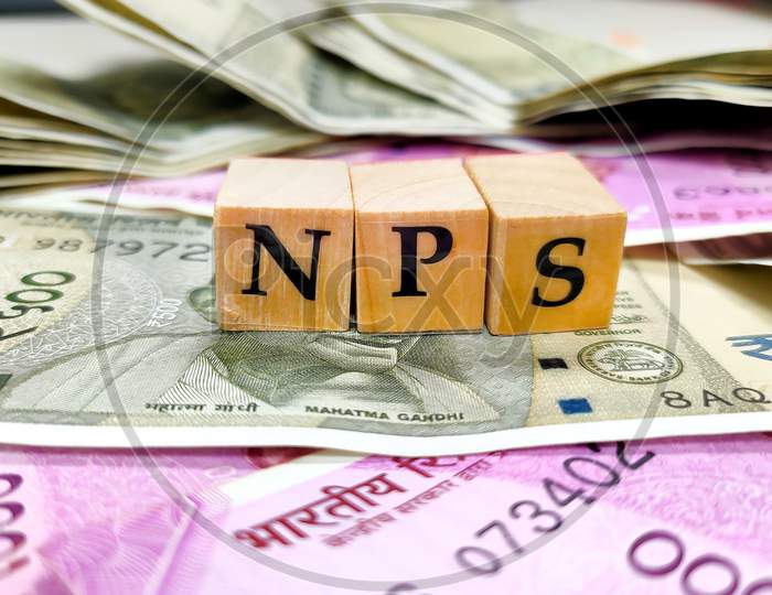 Nps Or National Pension Scheme With Wooden Bids Or Blocks On Indian Rupees Notes.