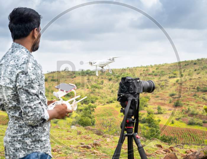 Focus On Drone, Young Videographer Filming Video By Controlling Drone Using Remote Controller - Concept Of Professional Drone Photography And Aerial Filmmaker