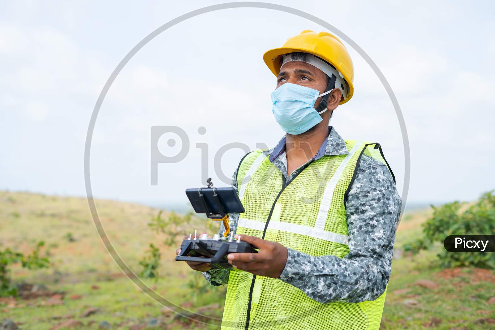 Drone Operator With Safety Helmet And Face Mask Operating Drone Using Remote Controller - Concept Of Engineer Doing Aerial Survey Using Uav During Coronavirus Covid-19 Pandemic