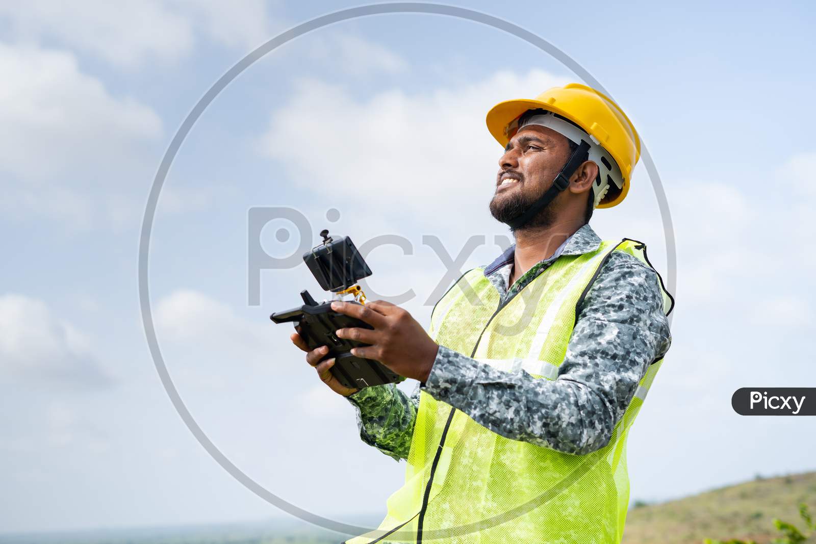 Drone Pilot With Safety Helmet Operating Drone Using Remote Controller - Concept Of Engineer Using Drone Technology To Survey Land.