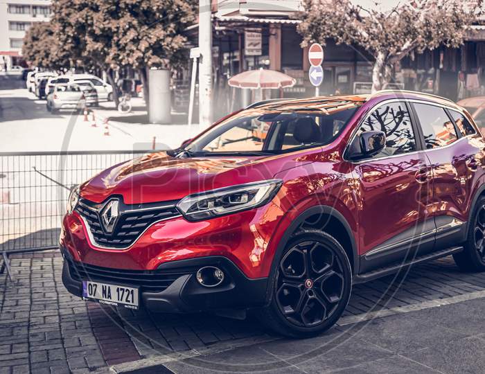 Alanya, Turkey – April 12 2021:     Red  Renault Captur   Parked  On The Street In City Against The Backdrop Of A   Buildung,  Shops, Trees