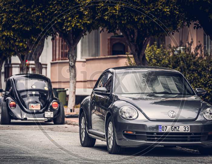 Alanya, Turkey – April 12 2021:   Two Vintage Black Volkswagen Beetle Cars Parked  On The Street In City Against The Backdrop Of A   Buildung,  Shops, Trees