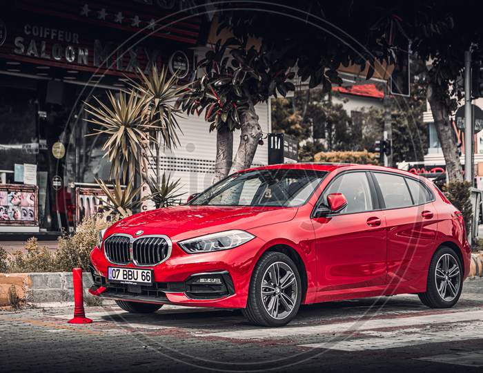 Alanya, Turkey – April 17 2021:   Red Bmw 1-Series Is Parked  On The Street In City Against The Backdrop Of A Buildung,  Shops