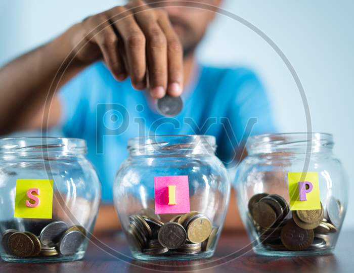 Focus On Jar, Man From Behind Placing Coins Inside The Jar - Concept Of Monthly Sip Or Systematic Investment Plan