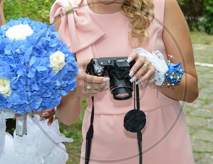 Portrait Of A Bride Holding A Blue Flower Bouquet Together With The Wedding Guests. The People Are Looking At Pictures In The Camera