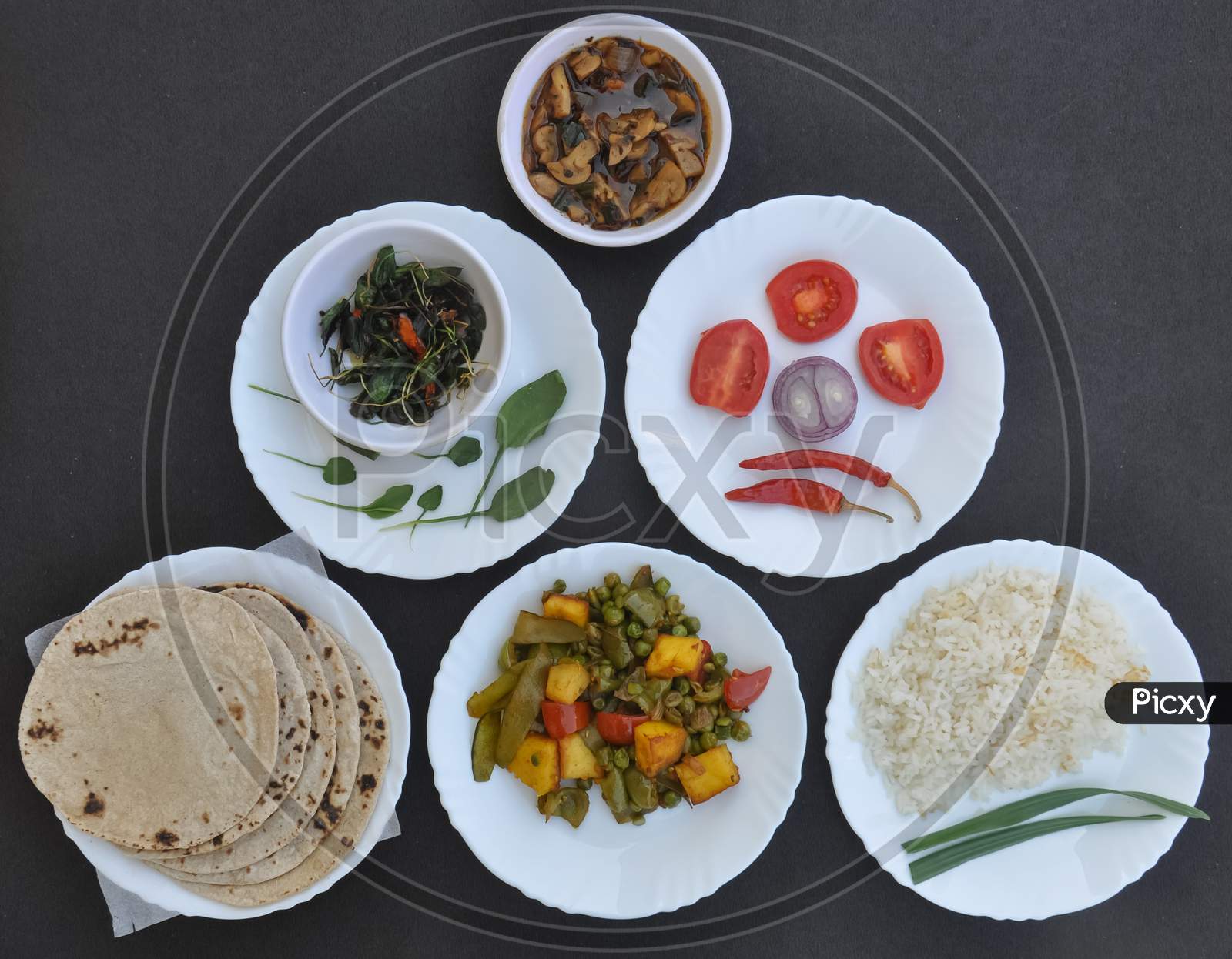 Indian Food - High angle view of mushroom soup, saag (greens), salad, roti (Indian bread), matar paneer mix veg and chawal (rice) in white plates over black background