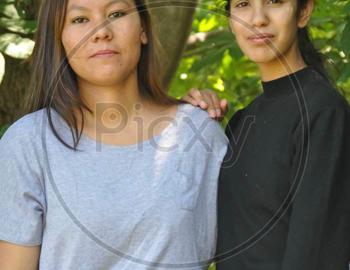 Portrait of two beautiful south asian young girls posing outdoors in against lesfy tree with looking at camera