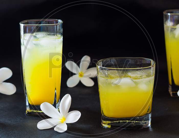 Selective focus on Fresh orange juice glass with ice . Front view with frangipani flowers and isolated on black background. Blur background.