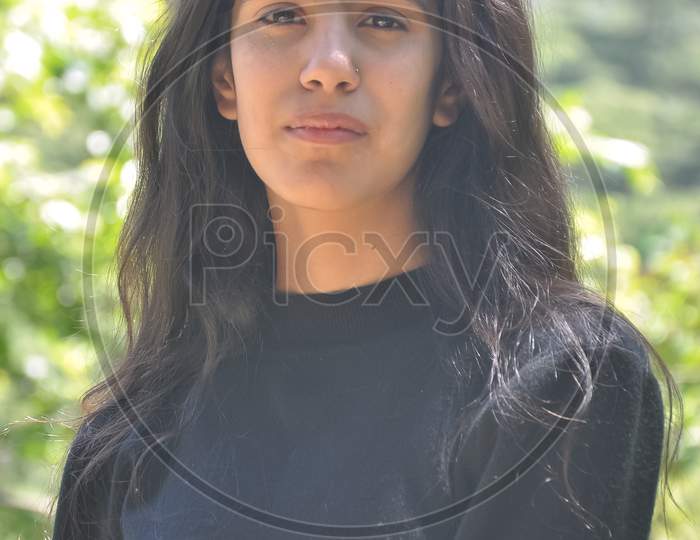 Closeup shot of a beautiful Indian young girl wearing black sweatshirt, posing outdoor in nature with looking at camera