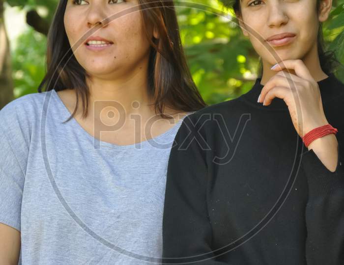Portrait of two beautiful south asian young girls posing outdoors in against lesfy tree with looking at camera