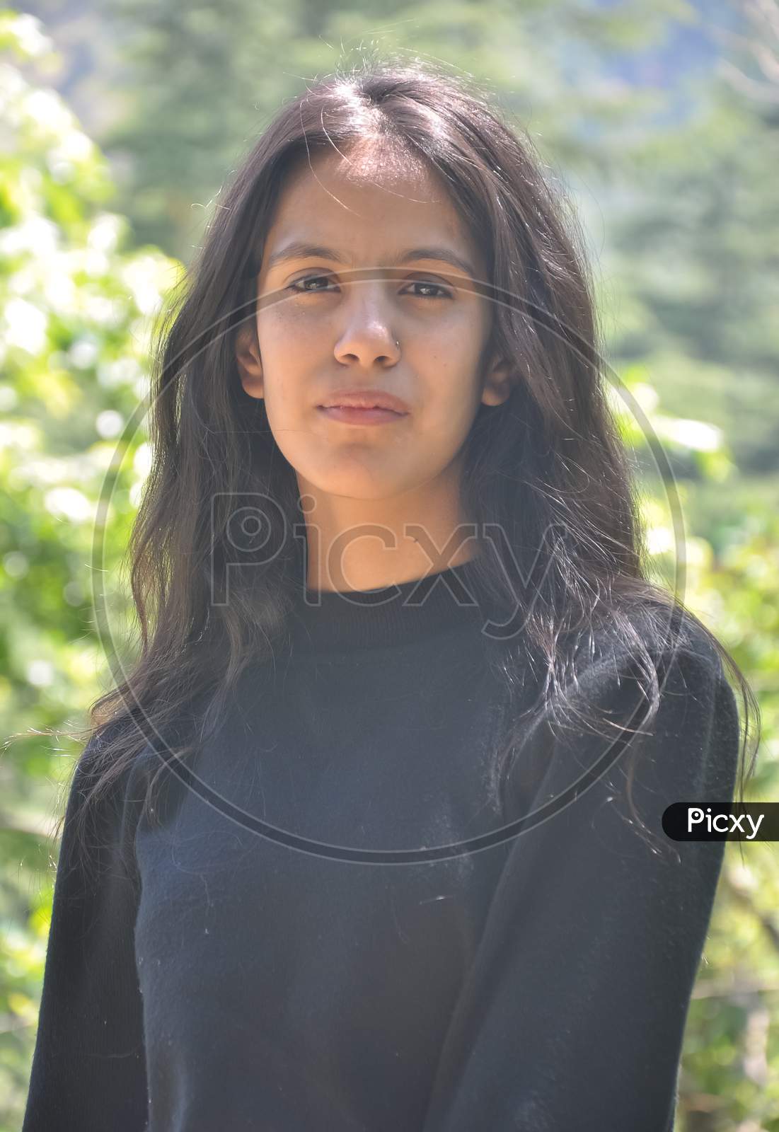 Closeup shot of a beautiful Indian young girl wearing black sweatshirt, posing outdoor in nature with looking at camera