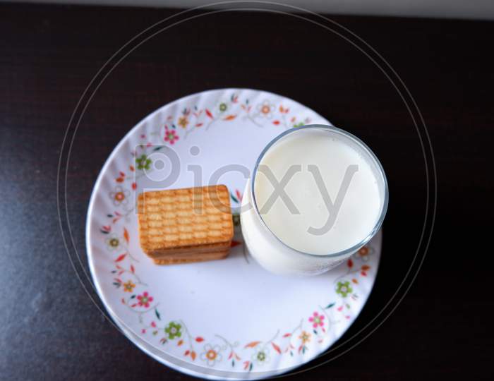 Glucose biscuits and Glass of milk served in white printed plate with black background