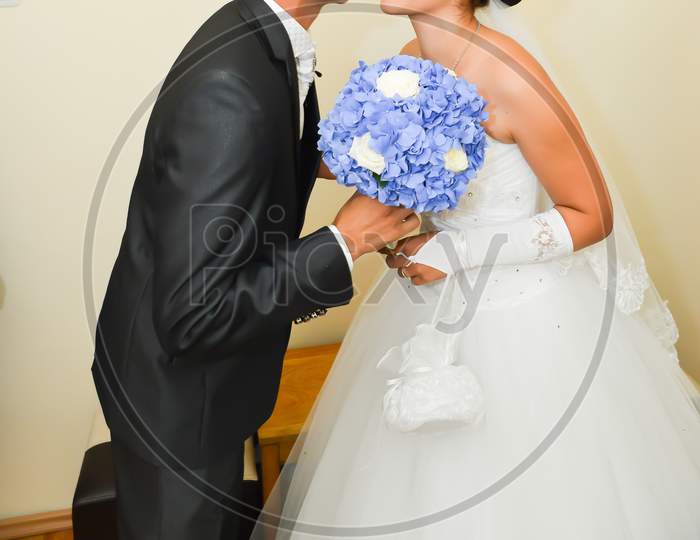 Bride And Groom Kissing Before The Wedding Ceremony. The Bride Is Holding A Blue Flower Bouquet