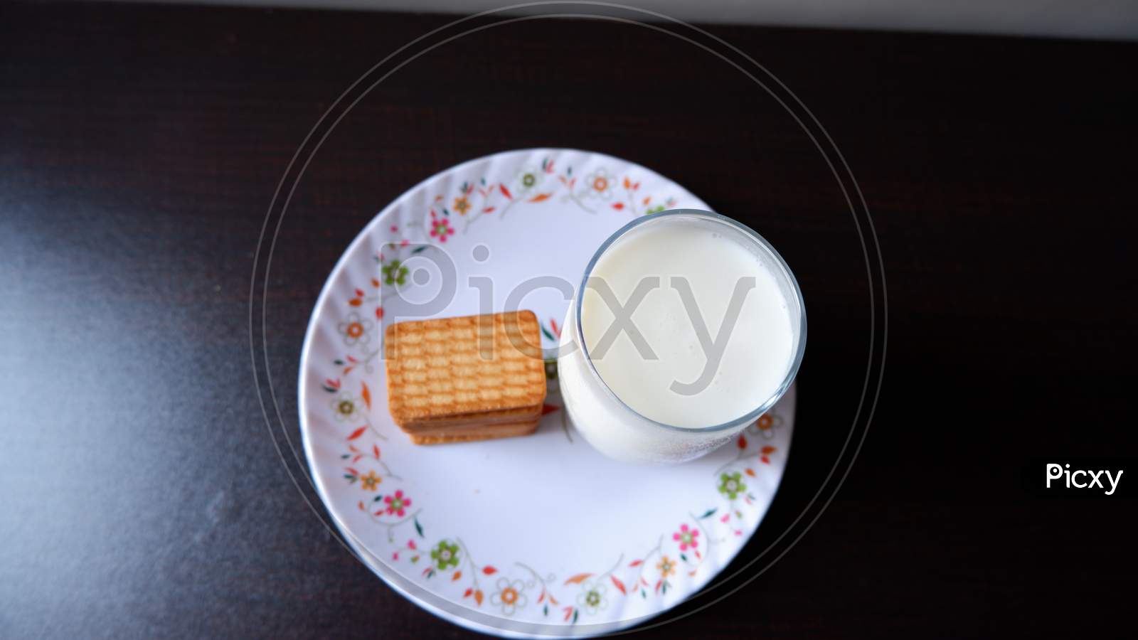 Glucose biscuits and Glass of milk served in white printed plate with black background