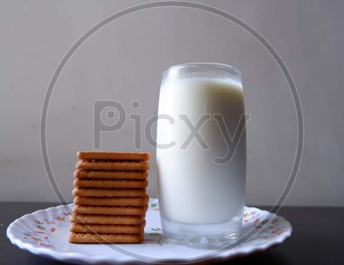 Side view of bunch of glucose biscuits and glass of milk on white plate