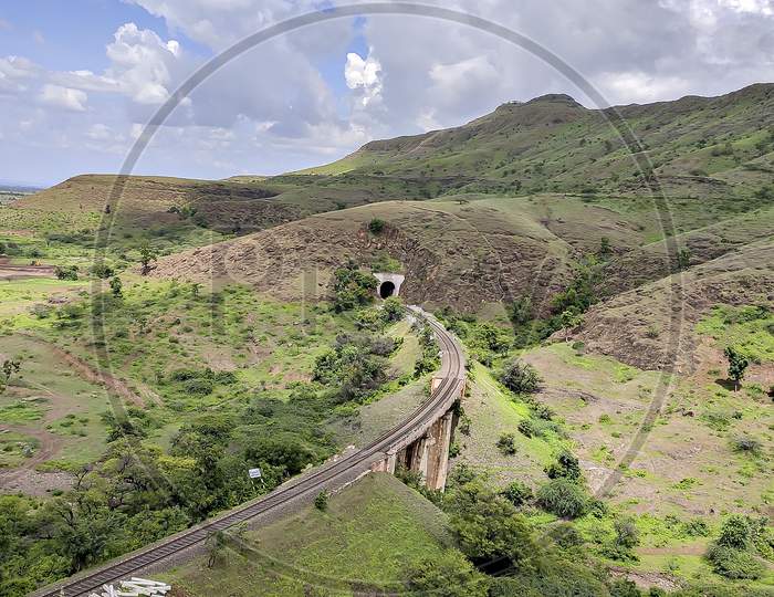 Single Railway Line Passing Through Tunnel In The Hill With Nice Blue Clouds Background.